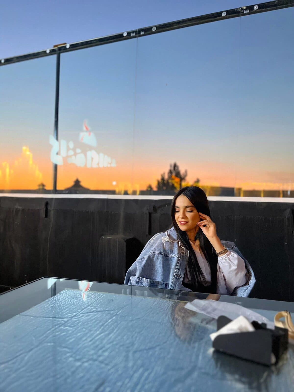 Zahra seated at a rooftop table against an orange sunset